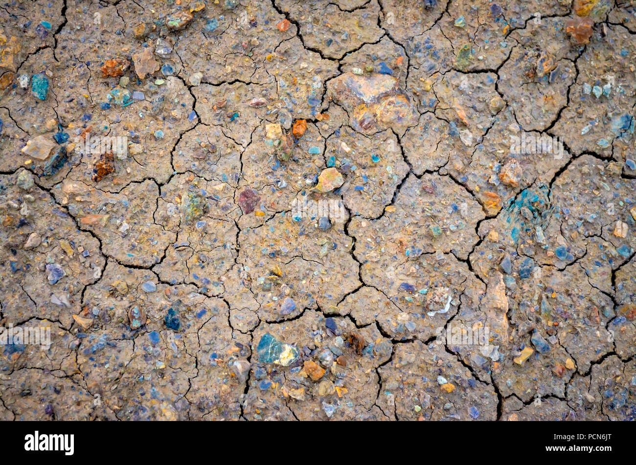Dried and cracked mud with colorful stones as background Stock Photo