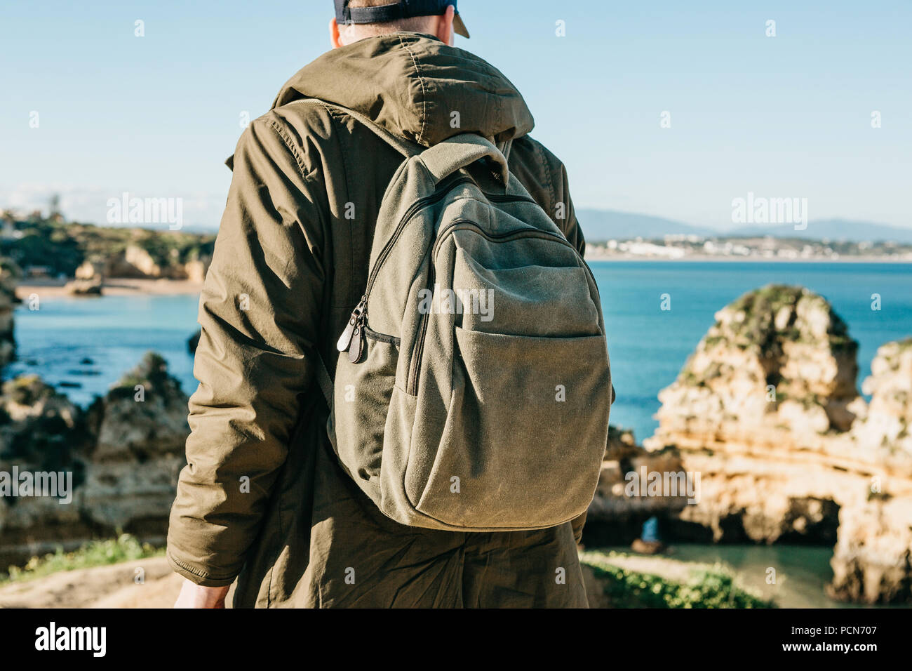 A tourist or traveler with a backpack admires the beautiful view of the Atlantic Ocean and the coast near the city called Lagos in Portugal. Stock Photo