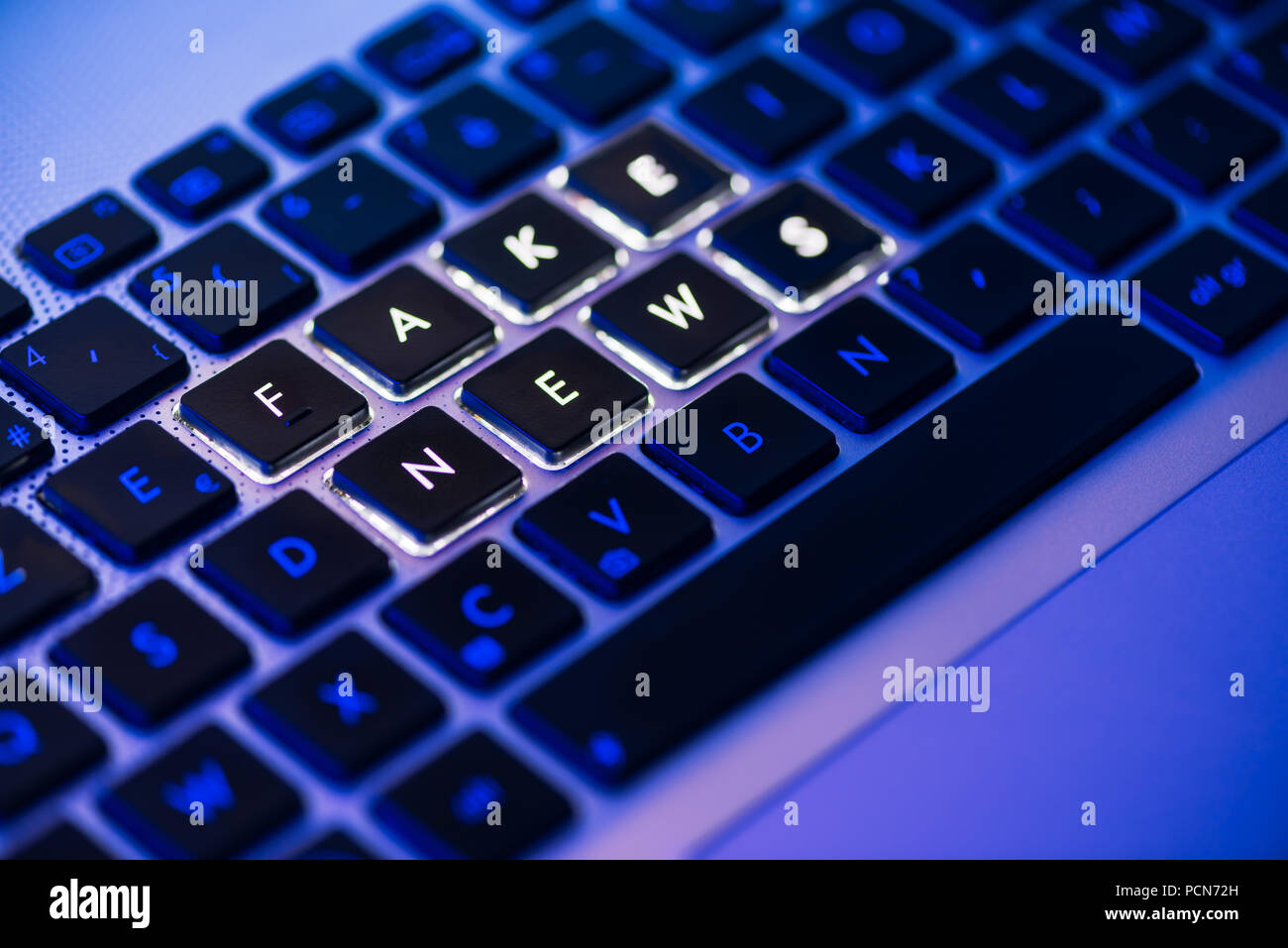 Fake news written on a backlit laptop keyboard close-up with selective focus in a blue ambiant light Stock Photo