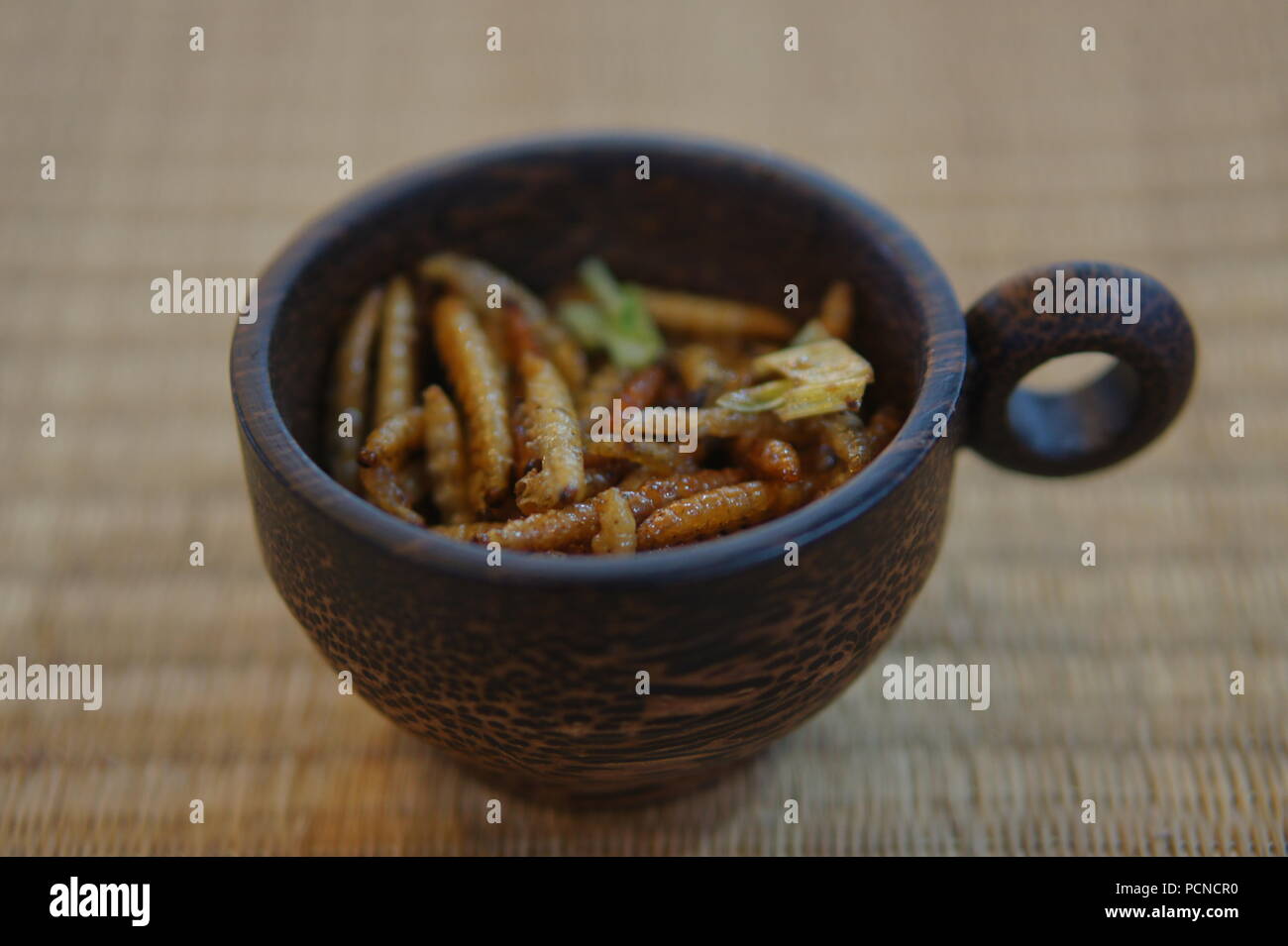 Edible Insects Bamboo Caterpillars in cup on a bamboo place mat Stock Photo