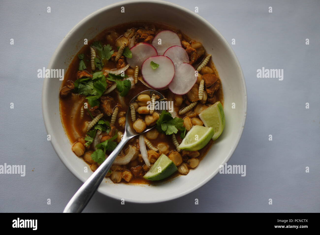Pozole (Hominy), cilantro (coriander), jalapeno peppers, onions, pork, lime, and pork with wax moth larvae Stock Photo