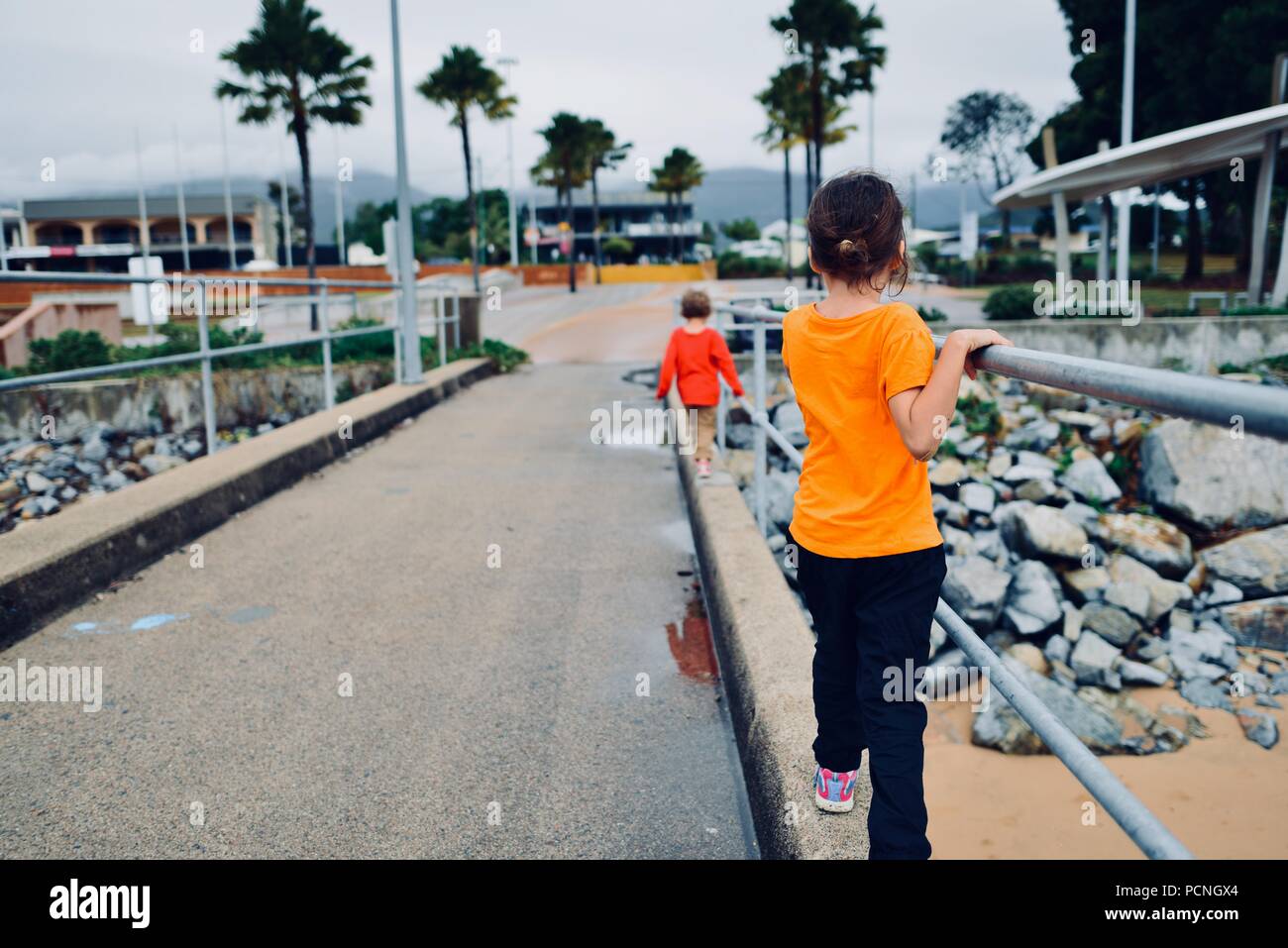 Children hanging off rails on a jetty as they walk, Cardwell ...