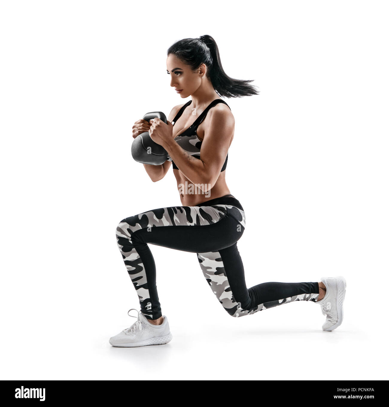 Athletic woman with kettlebell doing a lunges. Photo of latin woman in silhouette isolated on white background. Strength and motivation. Side view. Stock Photo