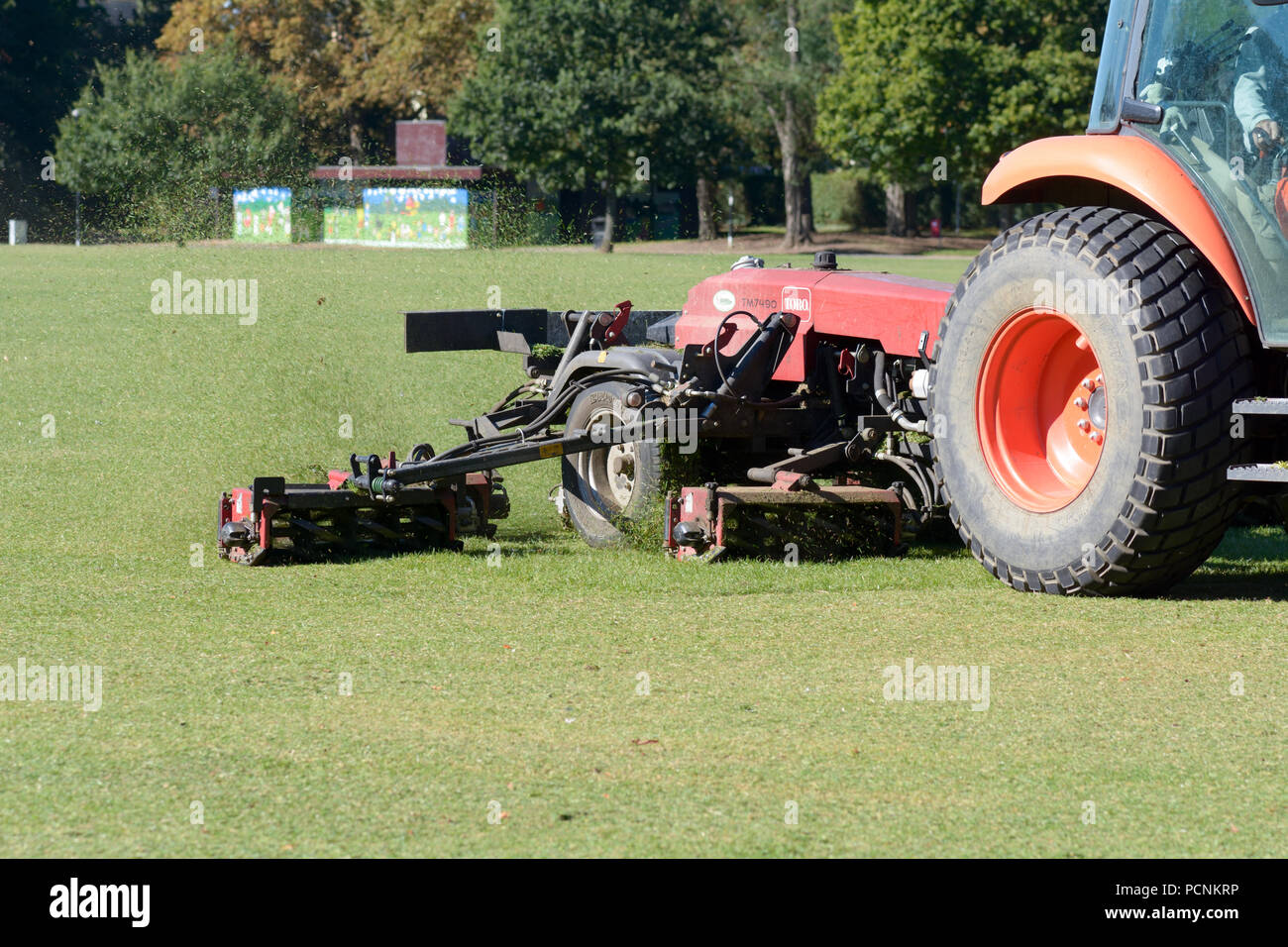 Tractor cutting grass in park that has been turned brown by the lack of rain Stock Photo