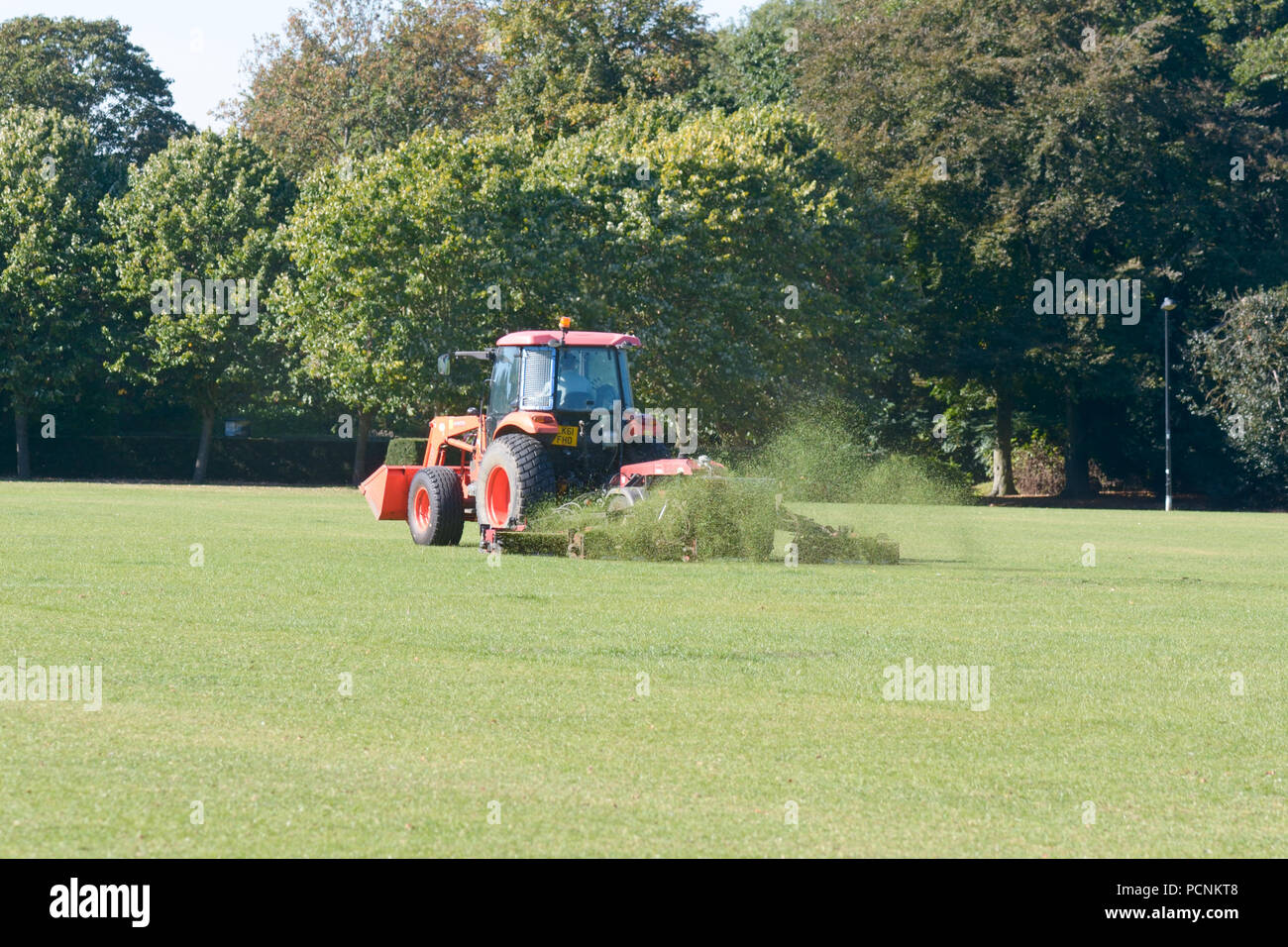 Tractor cutting grass in park that has been turned brown by the lack of rain Stock Photo