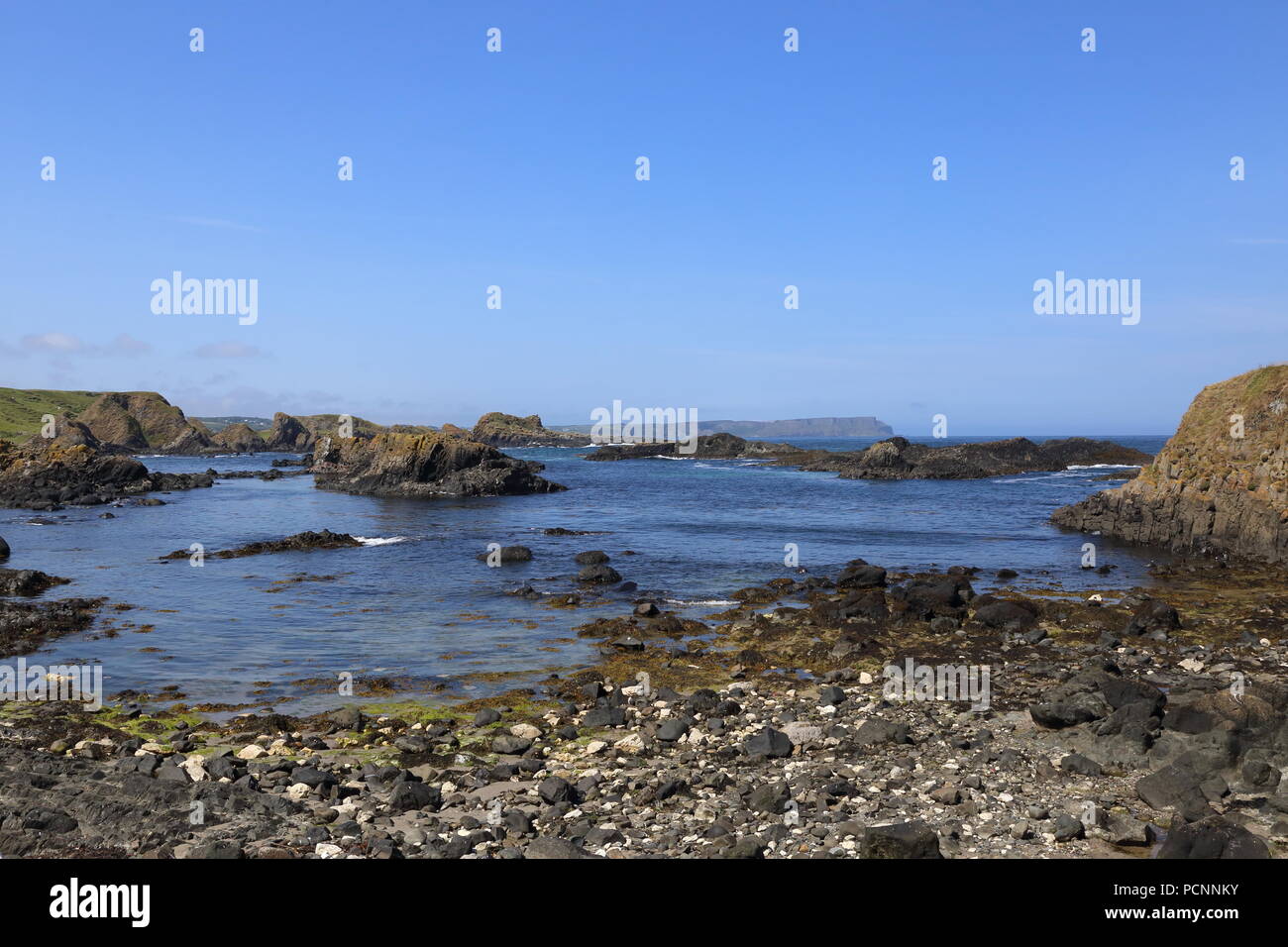 Small islets or skerries exposed by low tide at Ballintoy on the Causeway coast of Northern Ireland. Causeway head faintly visible in the distance. Stock Photo