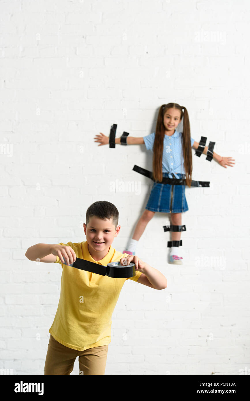 disobedient brother glued sister to wall with black tape at home Stock Photo