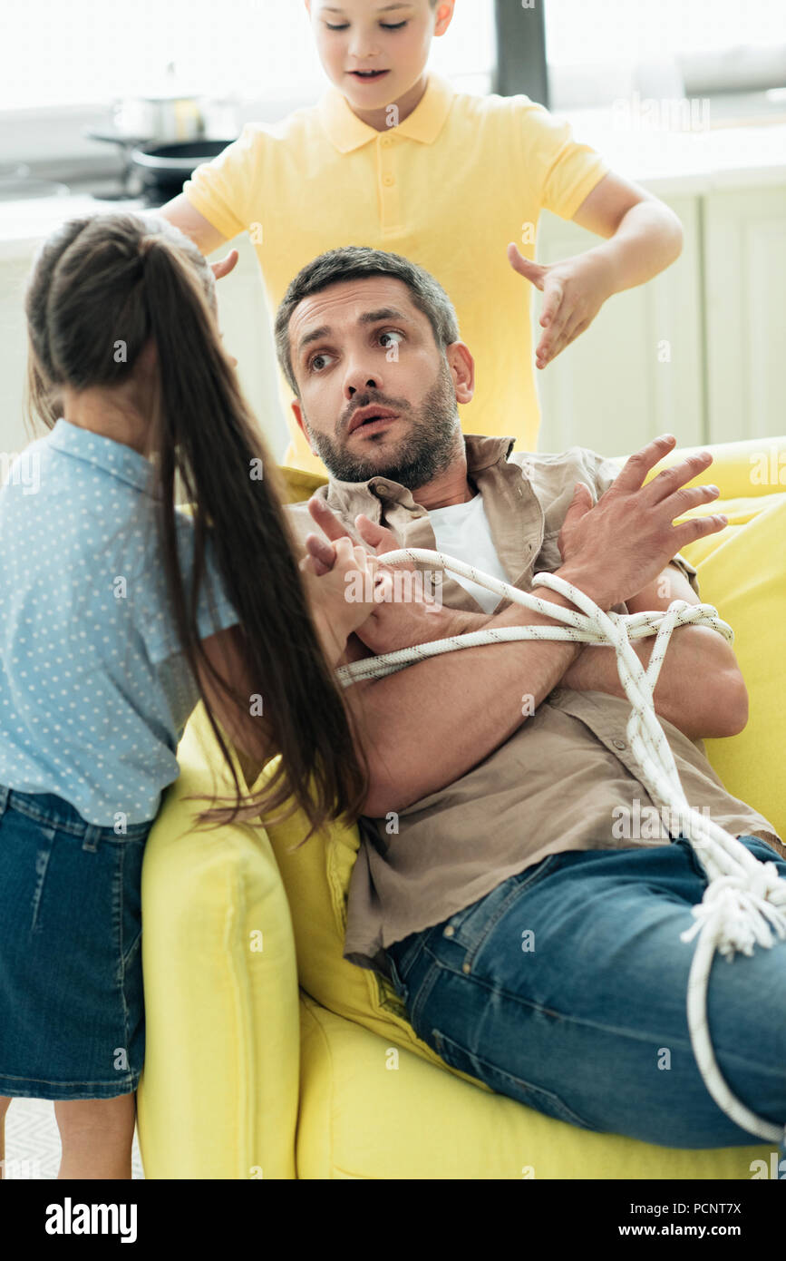 children tying father with rope at home, parenthood concept Stock Photo