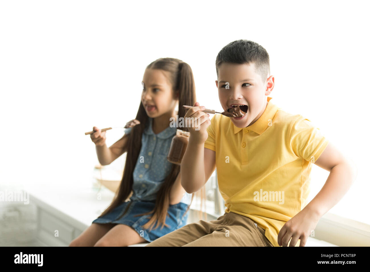siblings eating chocolate together in kitchen Stock Photo