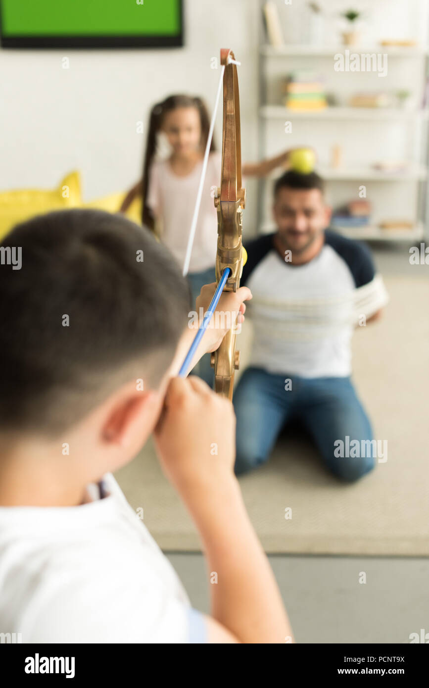 selective focus of children playing with tied father and pretending shooting with toy bow at home Stock Photo