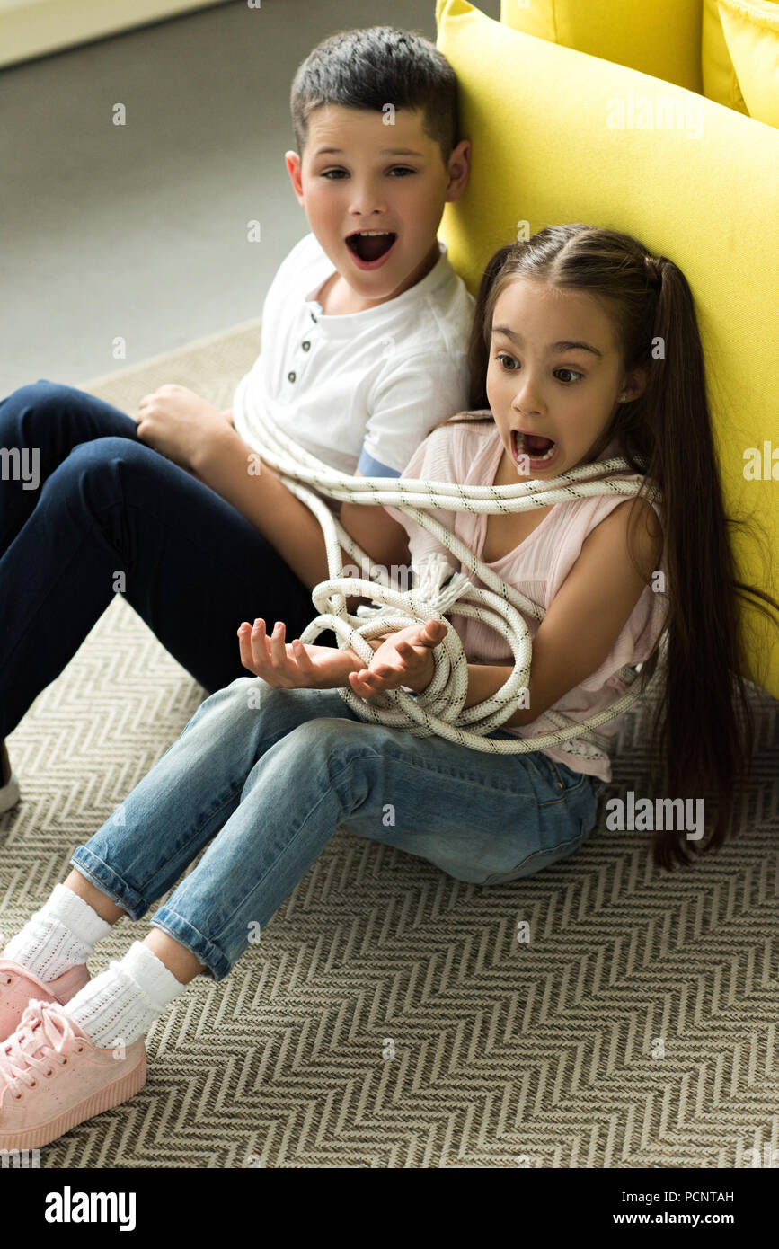tied with rope sister and brother sitting on floor and screaming at home Stock Photo