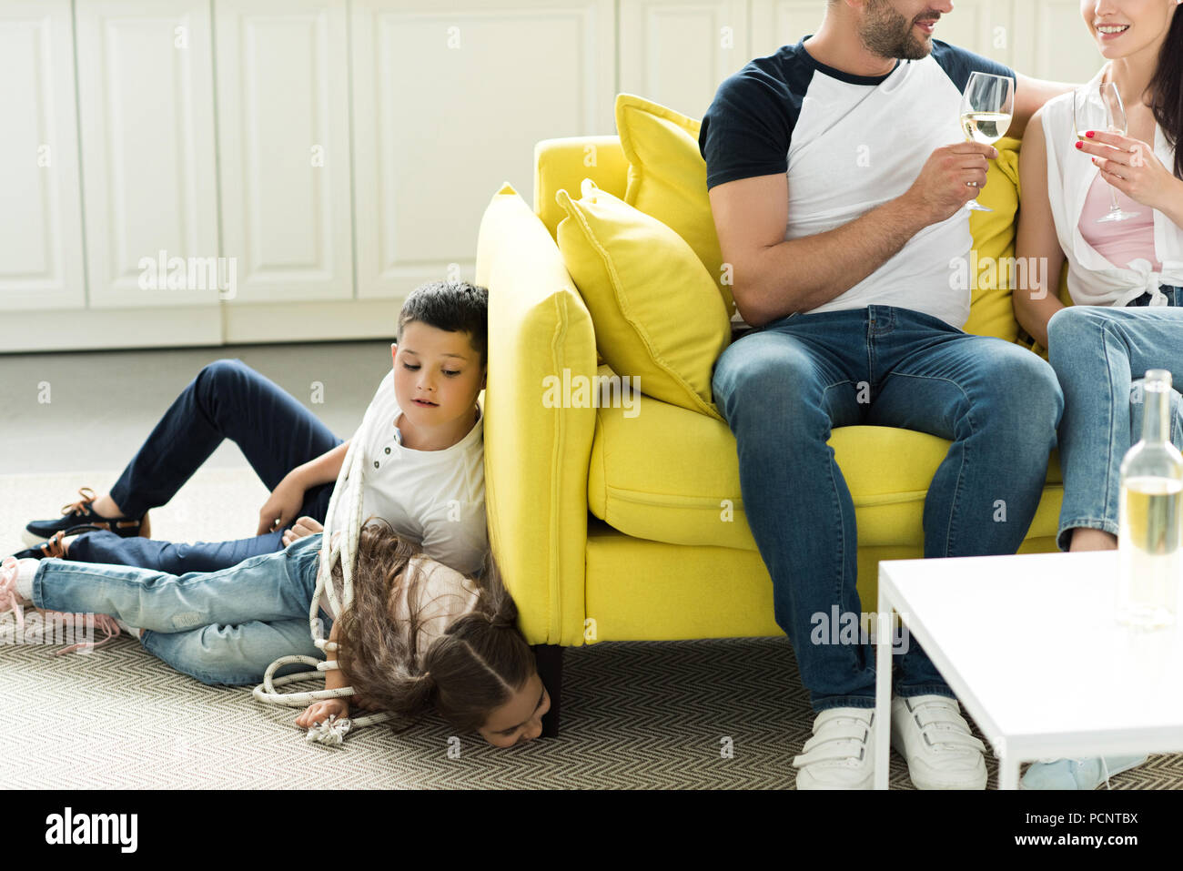 parents drinking wine and tied children lying on floor at home, parenthood concept Stock Photo
