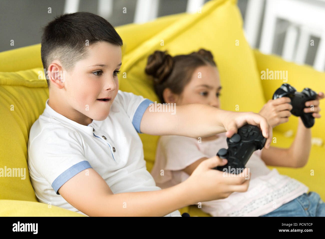 siblings playing video game on sofa at home Stock Photo