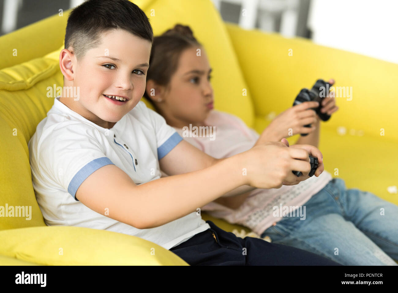 sister and brother playing video game on sofa at home Stock Photo