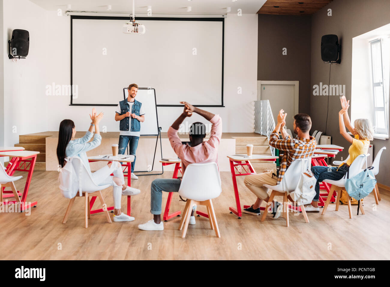 rear view of multiethnic young students clapping to lecturer after presentation at college Stock Photo