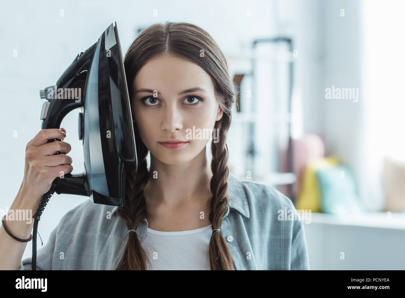 beautiful girl with braids holding iron near head Stock Photo
