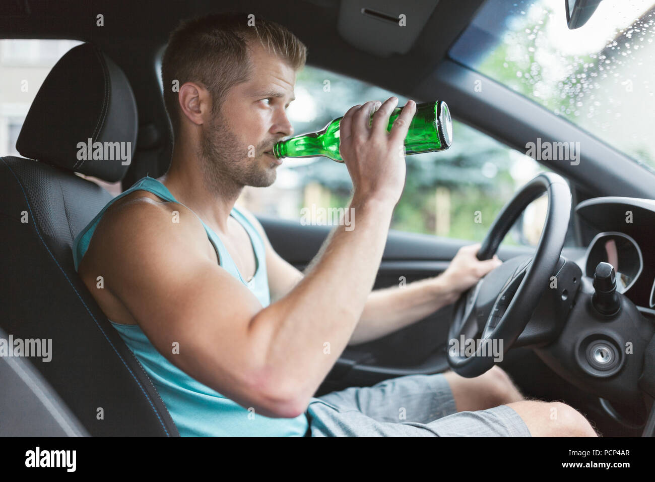 Drunk driver drinking behind the steering wheel of a car Stock Photo