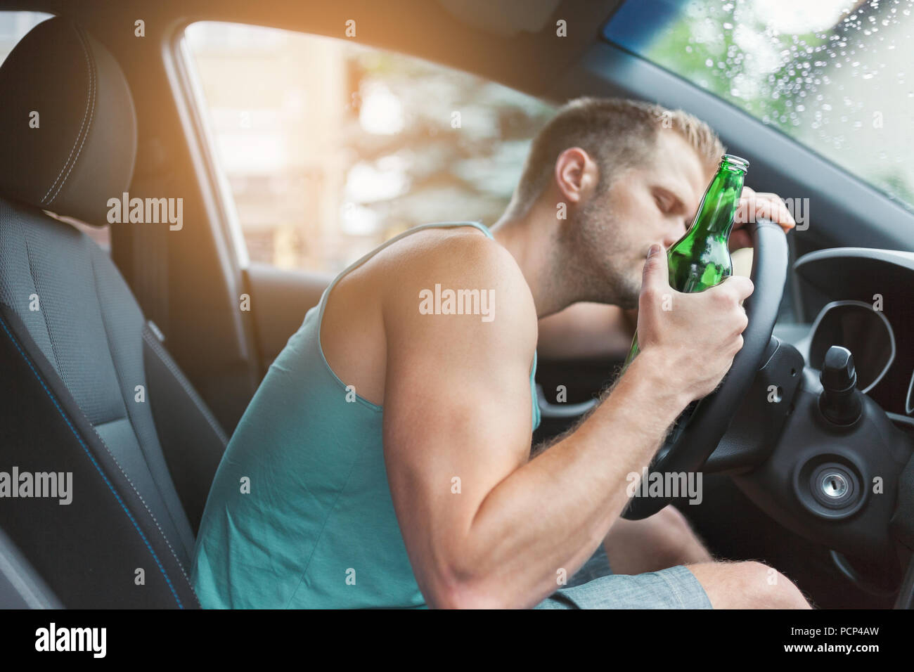 Drunk driver drinking behind the steering wheel of a car Stock Photo