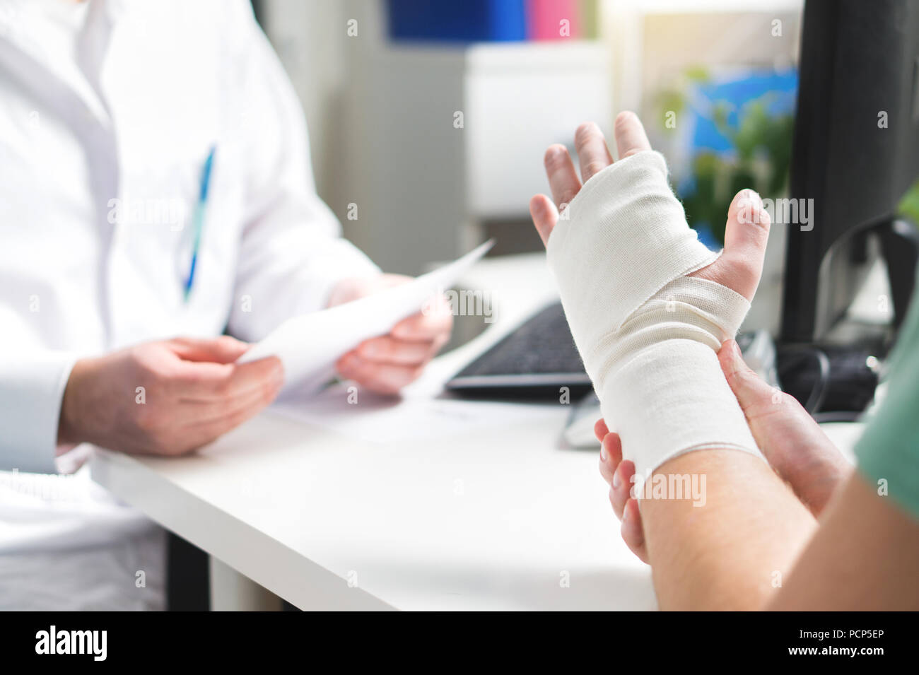 Injured patient showing doctor broken wrist and arm with bandage in hospital office or emergency room. Sprain, stress fracture or repetitive strain. Stock Photo