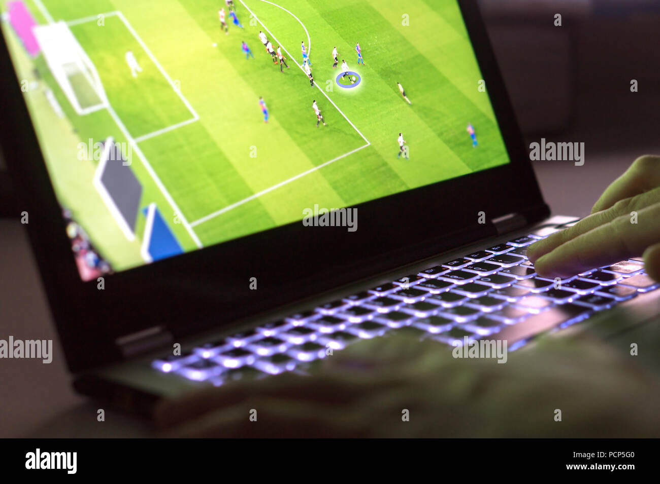 Young man playing video game with laptop. Online soccer or football game in computer. Close up of hands on computer keyboard. Stock Photo