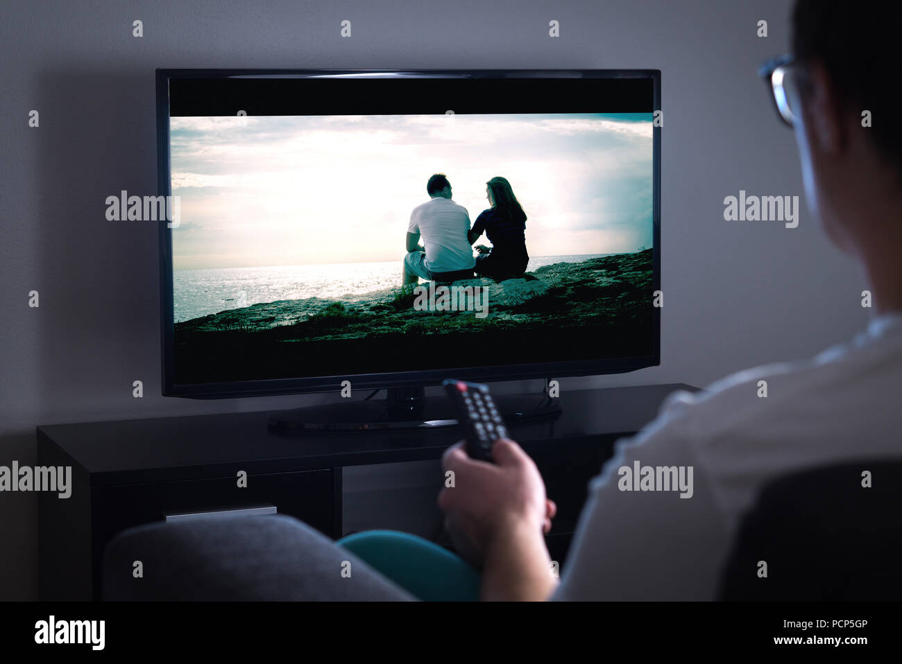 Man watching tv or streaming movie or series with smart tv at home. Film or show on television screen. Person holding the remote control. Stock Photo