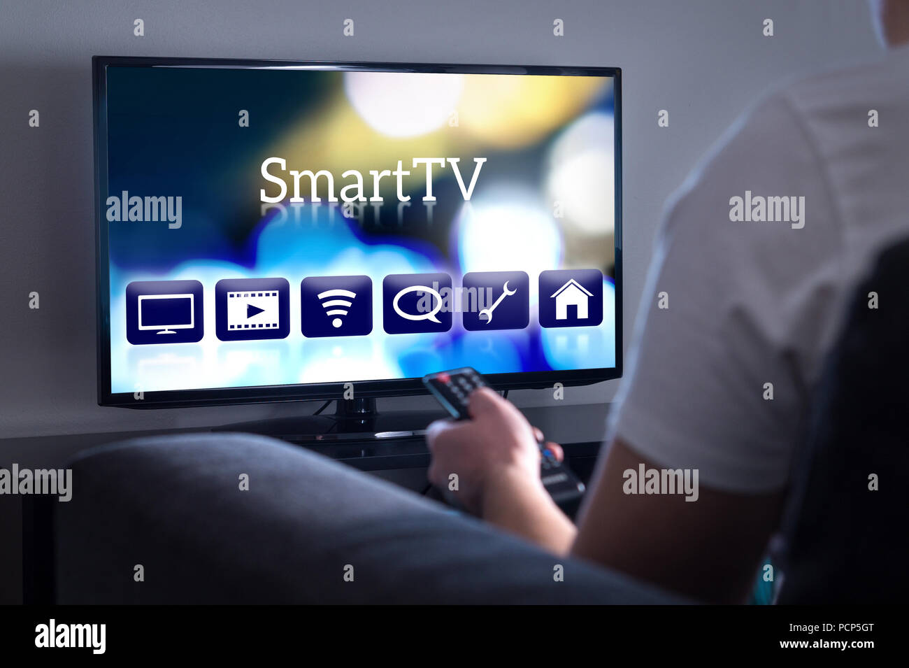 Man watching smart tv. Choosing movie or series from the menu. Person holding remote control. User interface on television screen. Stock Photo
