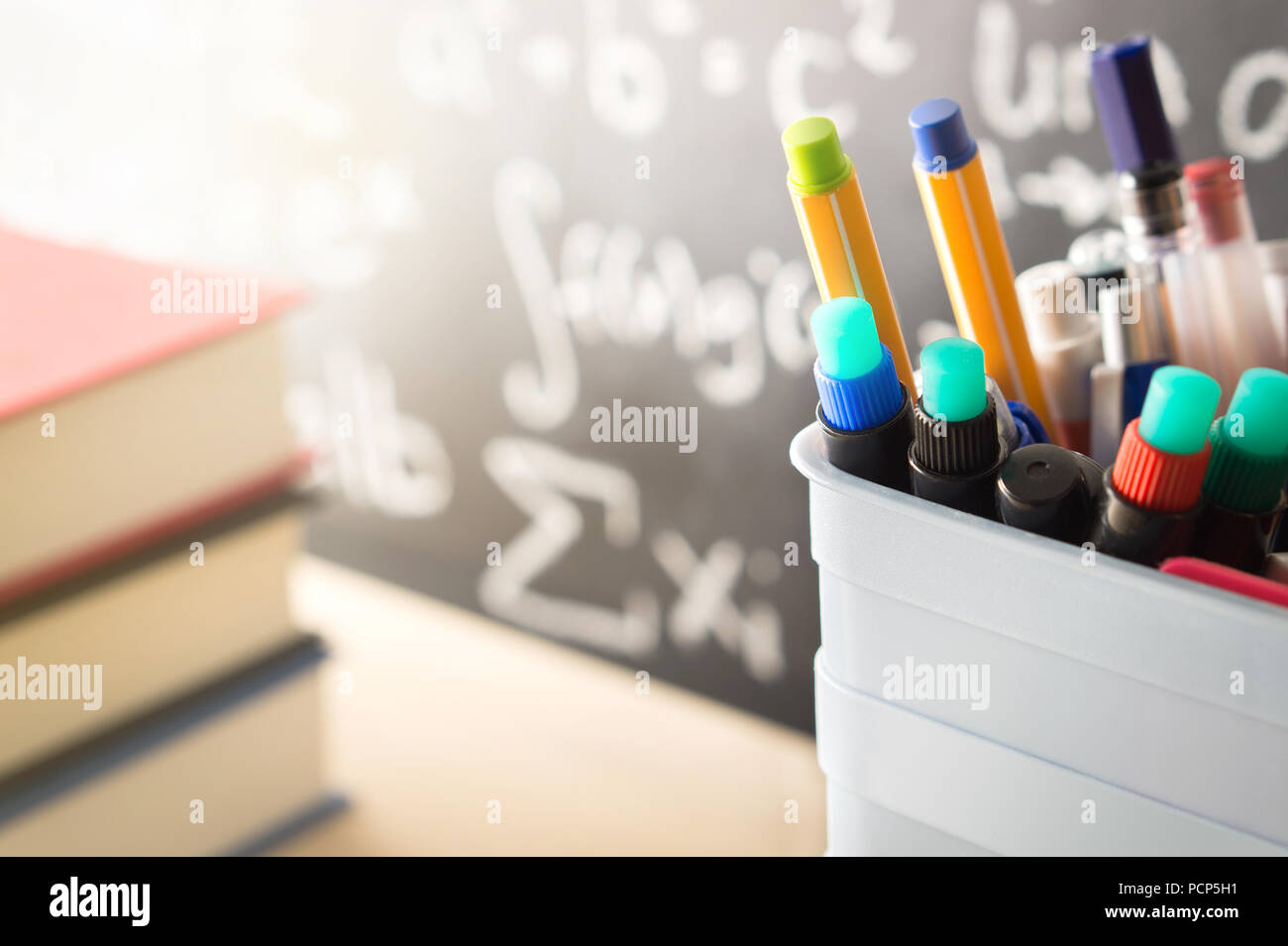 Pen holder and books in front of blackboard in classroom. Education, learning, teaching and knowledge concept. Classroom with chalkboard. Stock Photo