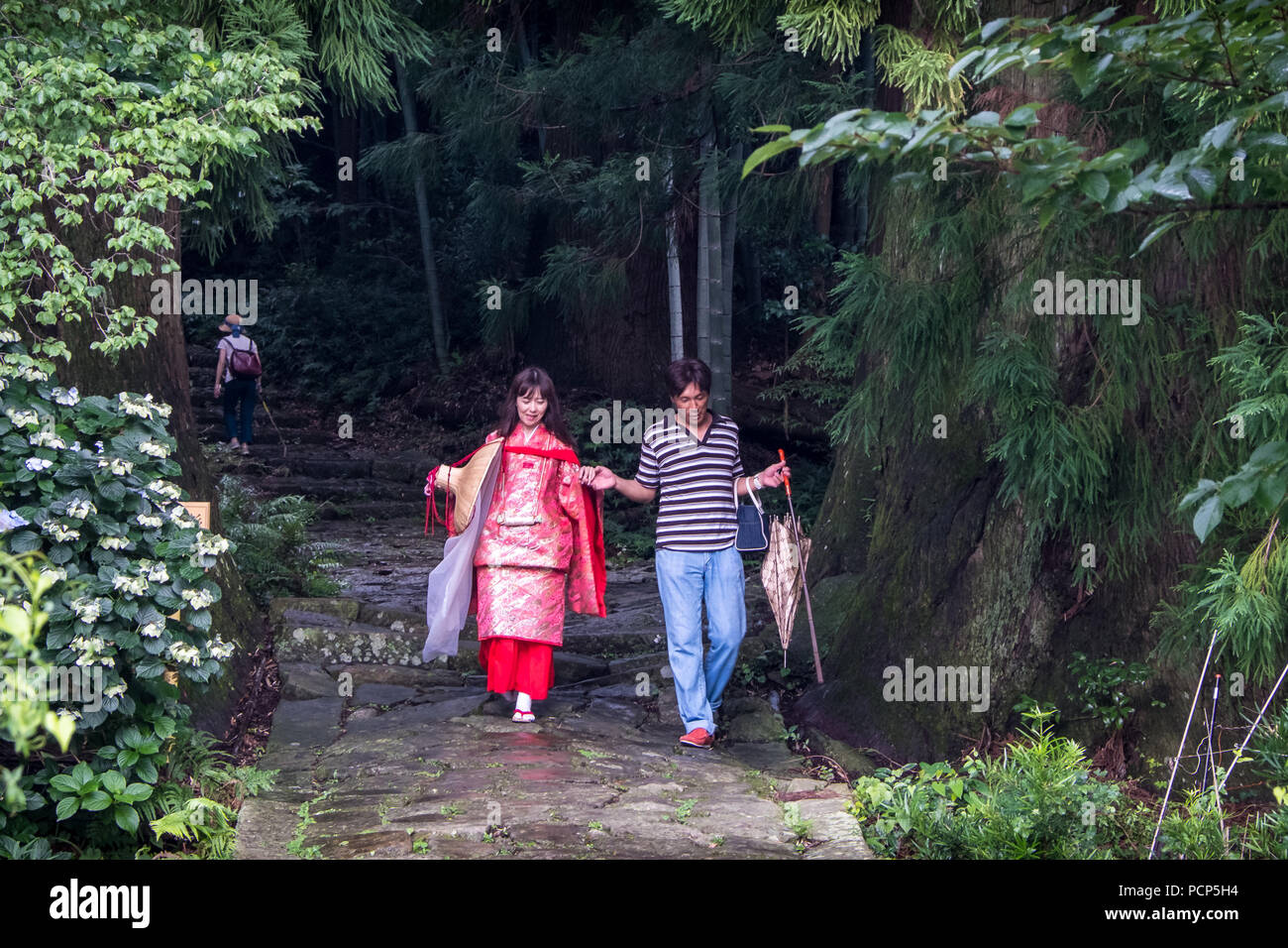The ancient pelgrim path Daimonzaka, part of the Kumano Kodo, near Nachisan in Japan, with the woman wearing the traditional pelgrim costume. Stock Photo