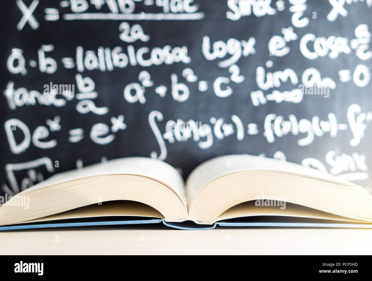 Knowledge, education, mathematics, science and wisdom concept. Open book in front of a blackboard and chalkboard full of math writing. Stock Photo