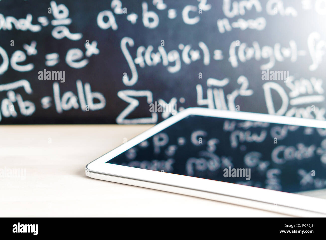 Modern education and e learning concept. Tablet in front of a blackboard full of writing at school. Smart mobile device and chalkboard in classroom. Stock Photo