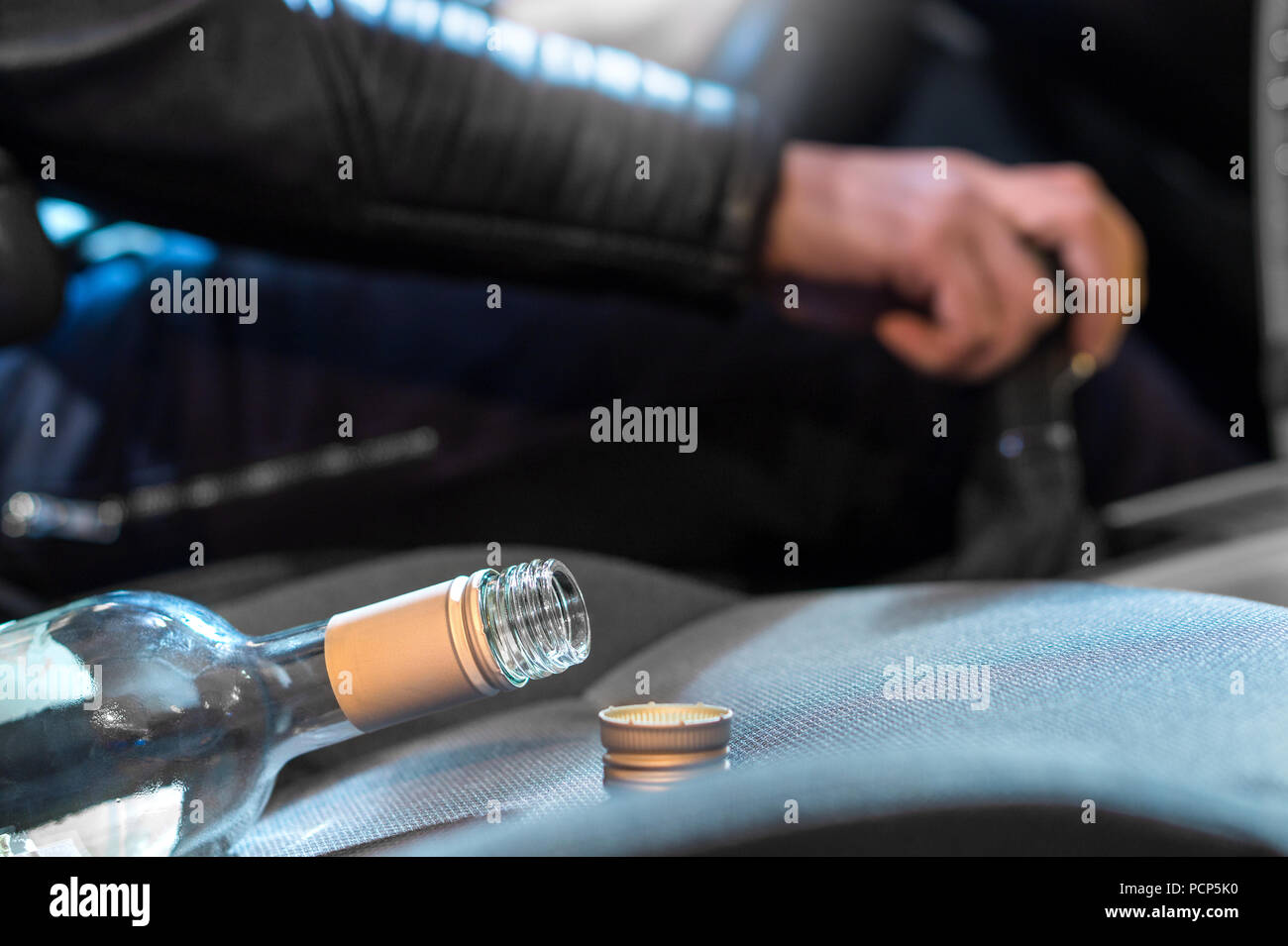 Drunk driving concept. Young man driving car under the influence of alcohol. Hand on gear stick. Close up of empty bottle of wine on front seat. Stock Photo