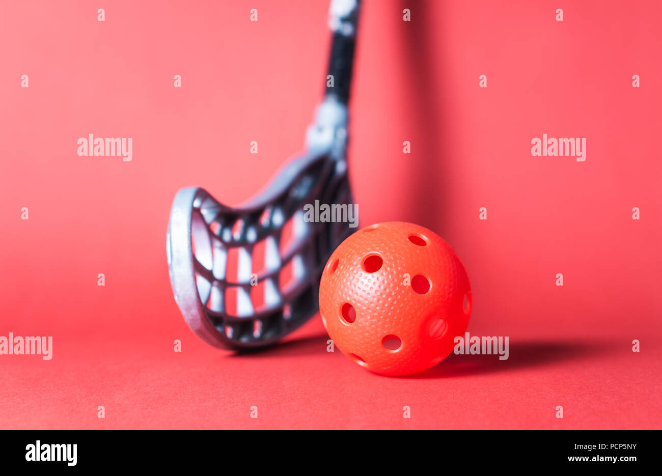 Floorball stick and ball against red background. Floor hockey concept. Stock Photo
