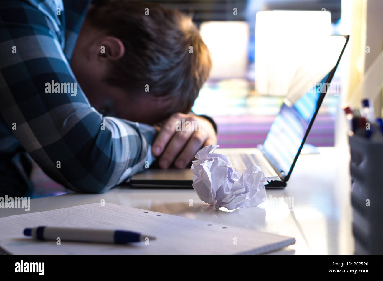 Sad and tired man in home or modern business office at night. Unemployed job seeker or businessman with ripped paper and laptop on table. Stock Photo