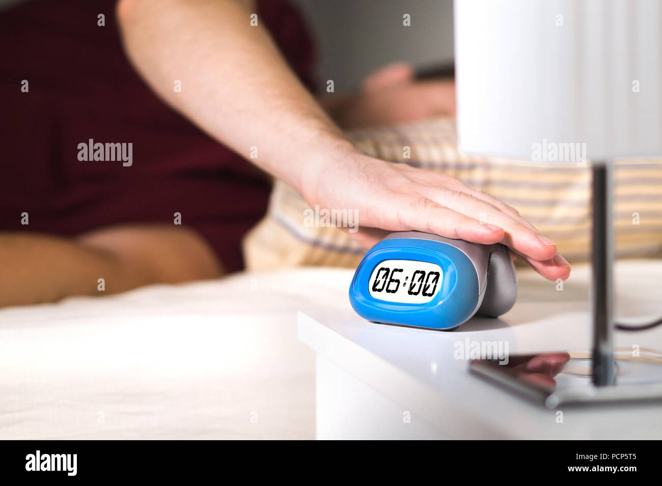 Man waking up in bed. Turning off alarm clock on nightstand or pressing