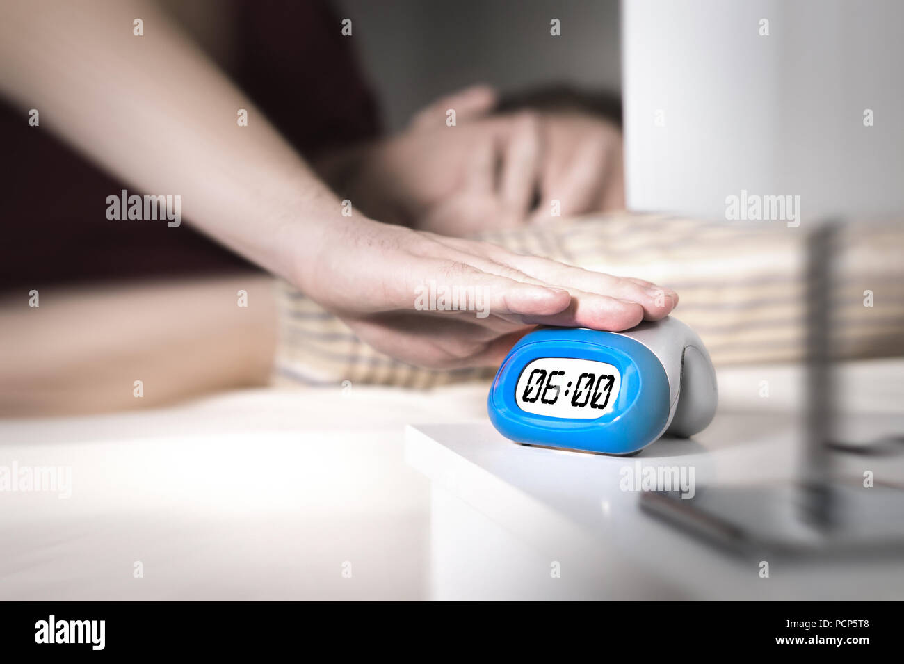 Man don't want to wake up for work in the morning. Turning off alarm clock or press snooze button with hand. Lazy person unable to get out of bed. Stock Photo