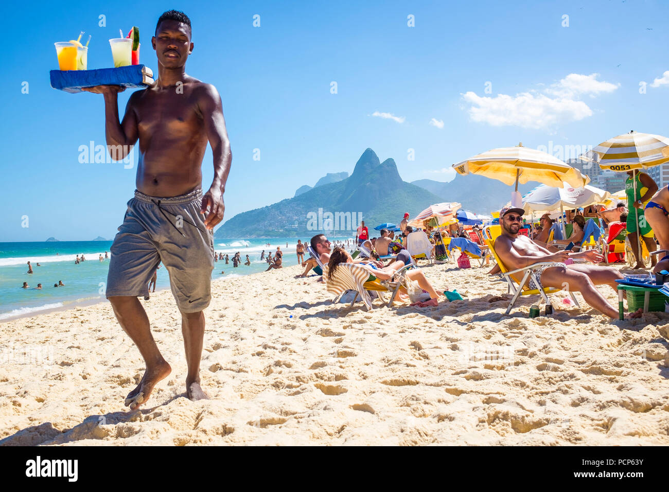 RIO DE JANEIRO - CIRCA MARCH, 2018: A beach vendor selling caipirinhas calls out to  customers on Ipanema Beach with Two Brothers mountain backdrop Stock Photo