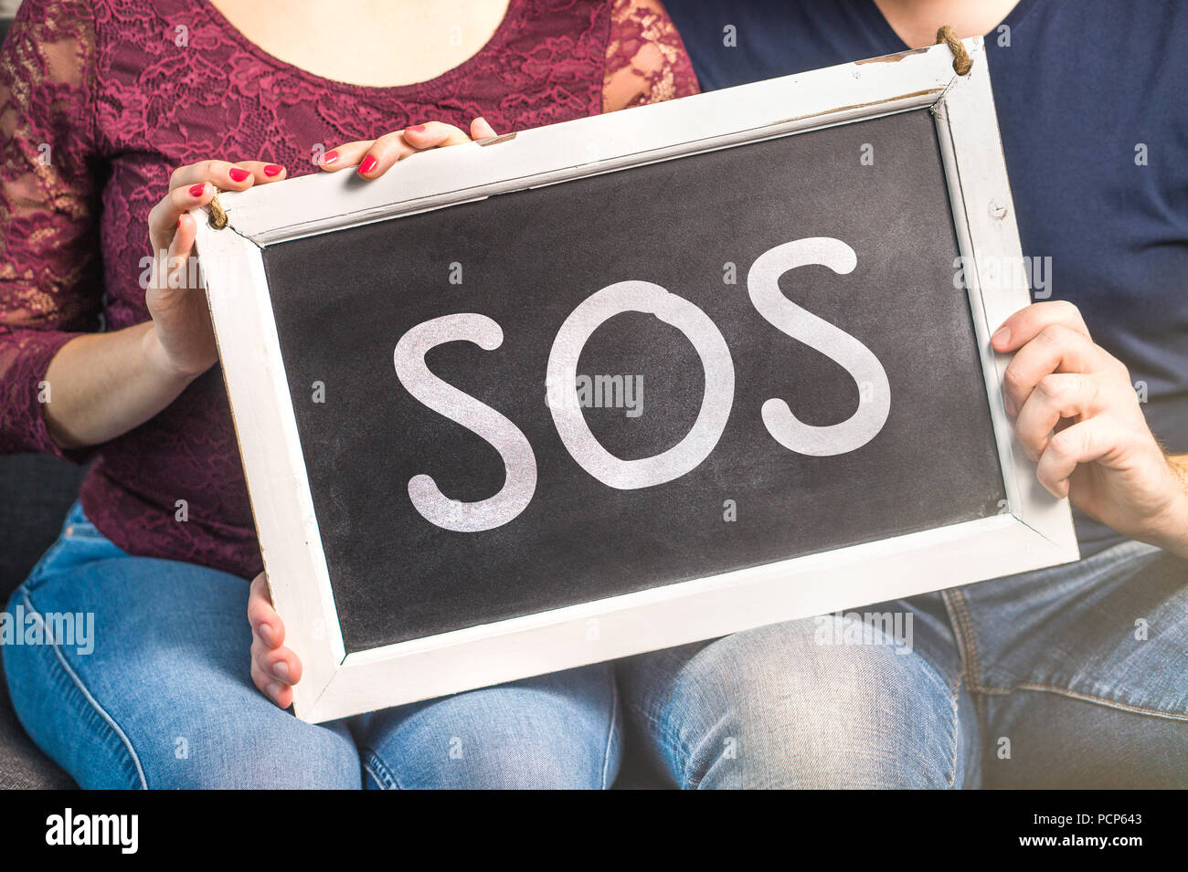 Couples therapy or marriage counseling concept. Needs help for relationship problems. Man and woman holding blackboard with SOS text. Stock Photo