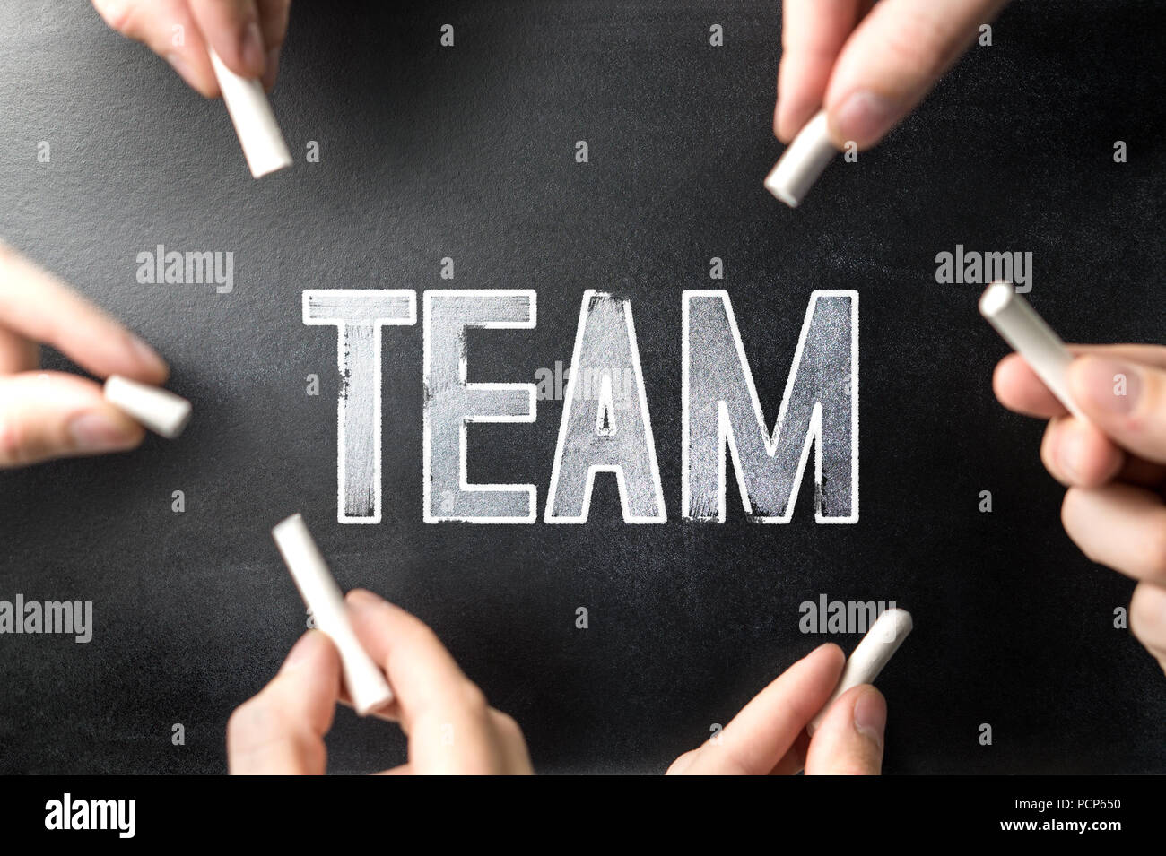 Teamwork and group work concept. Multiple people writing the word team to the same chalkboard with chalk pens. Stock Photo