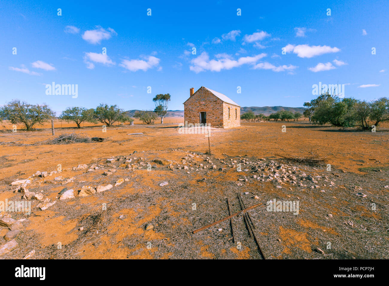 Old ruins among scarce trees under bright sun on orange dry land in South Australia Stock Photo