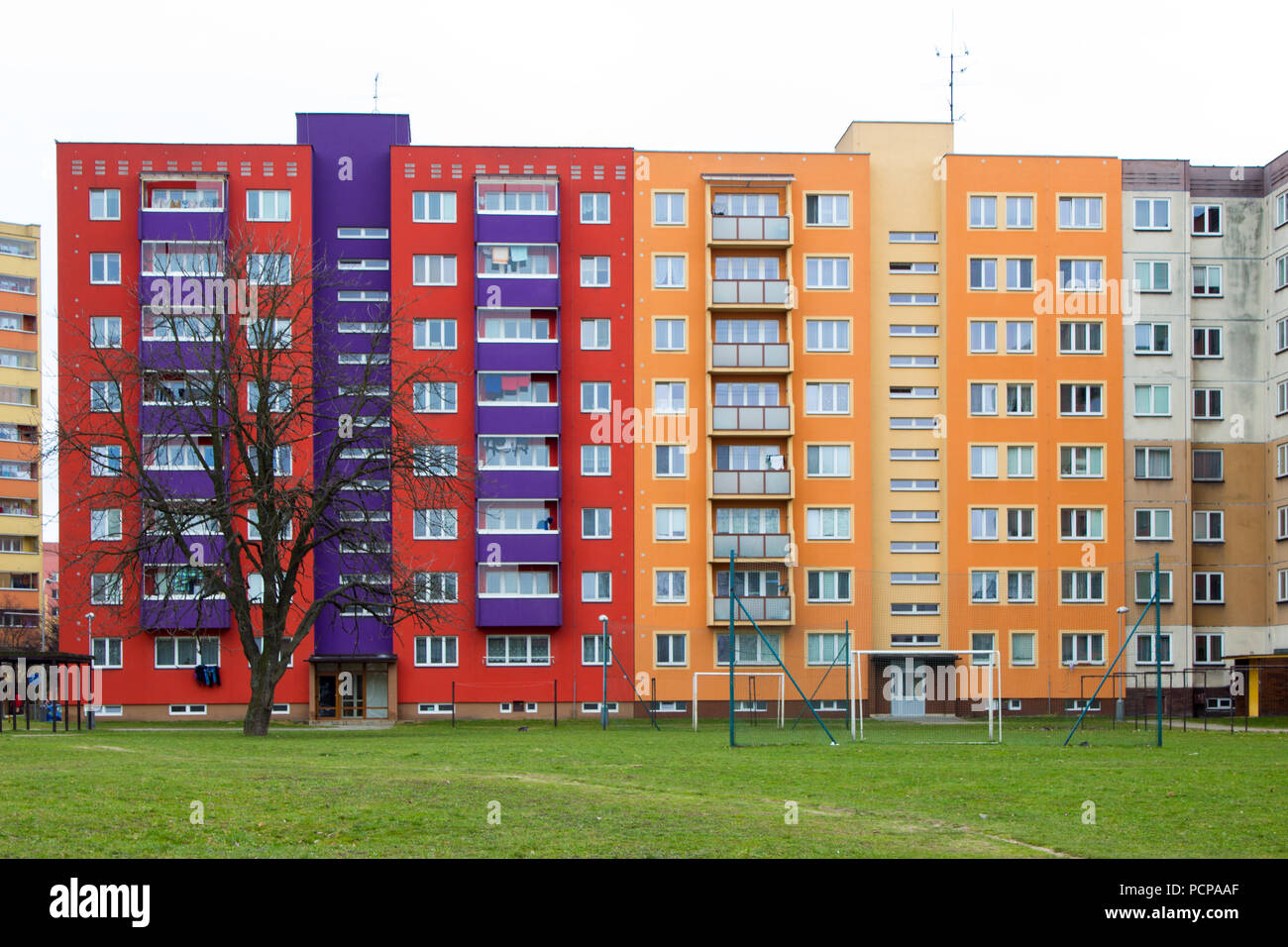 Red yellow orange and violet block of flats in Frydek Mistek in the Czech Republic. In the foreground is a park with grass and trees. Stock Photo