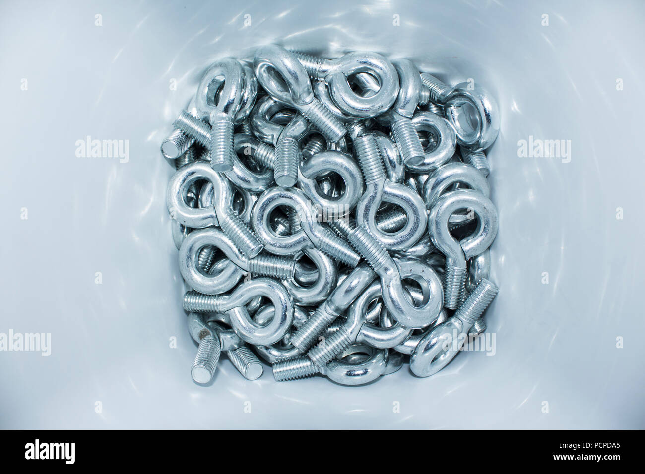 Lots of big industrial galvanized eye bolts on a pile in a white bucket Stock Photo