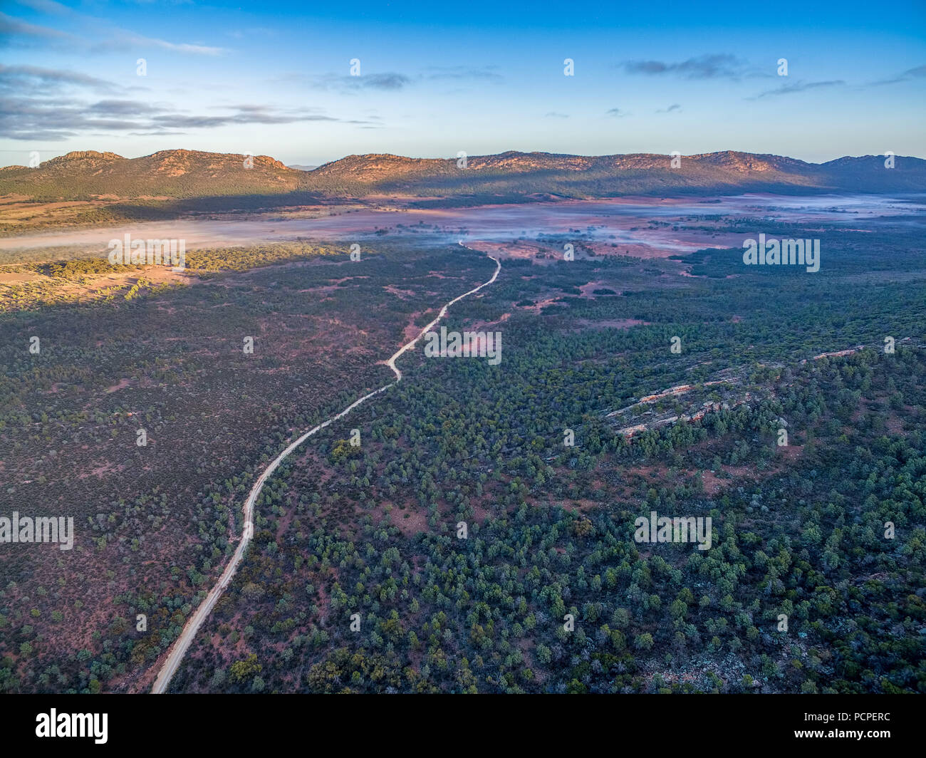 Aerial view of dirt road winding through South Australian outback landscape at sunrise. Stock Photo