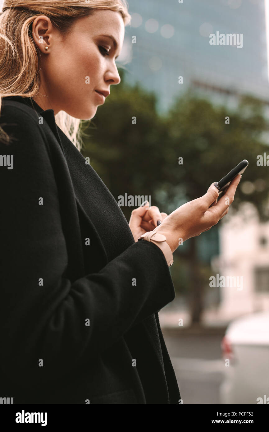 Young businesswoman requesting pickup by taxi on his phone via ride sharing application. Female commuter using online transportation service. Stock Photo