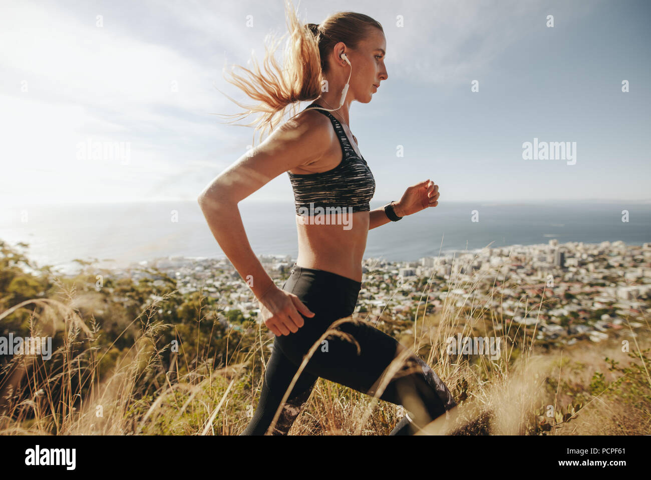 Side view of string young woman in sportswear running through extreme terrain on mountain. Female runner training for cross country run. Stock Photo