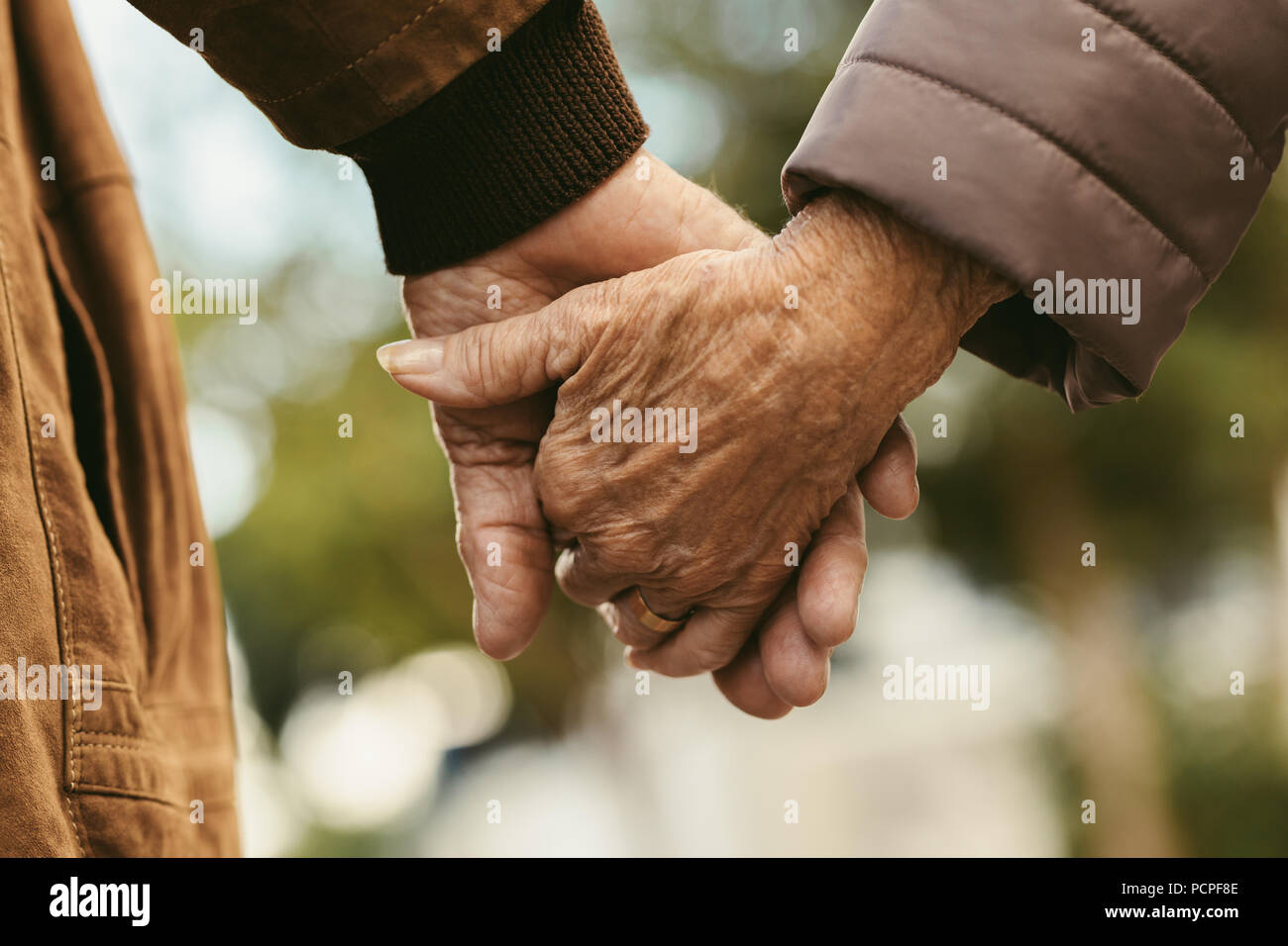 Close up of elderly couple holding hands and walking outdoors. Rear ...