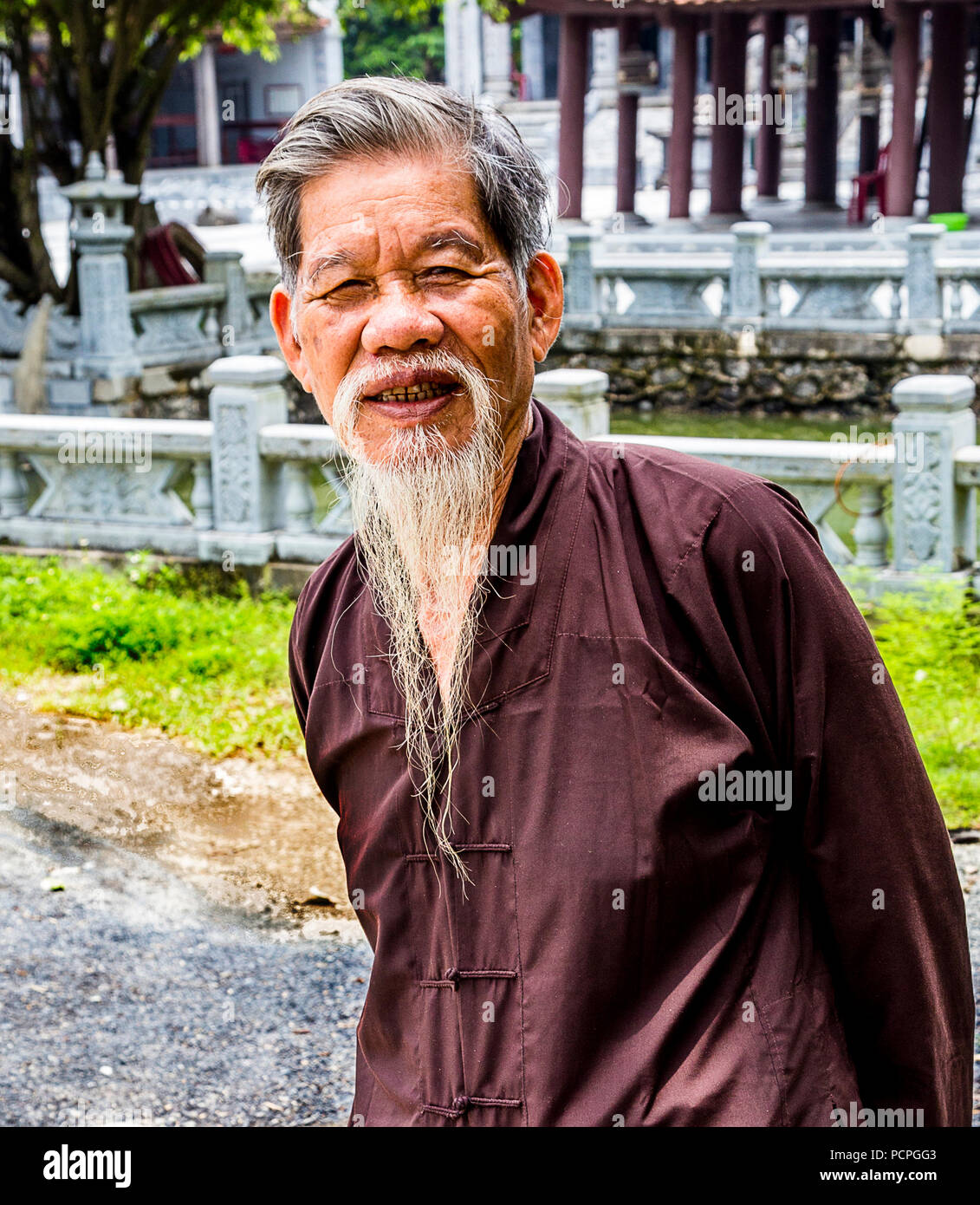 Old Vietnamese religious man with white beard and brown asian coat jacket shirt. Stock Photo