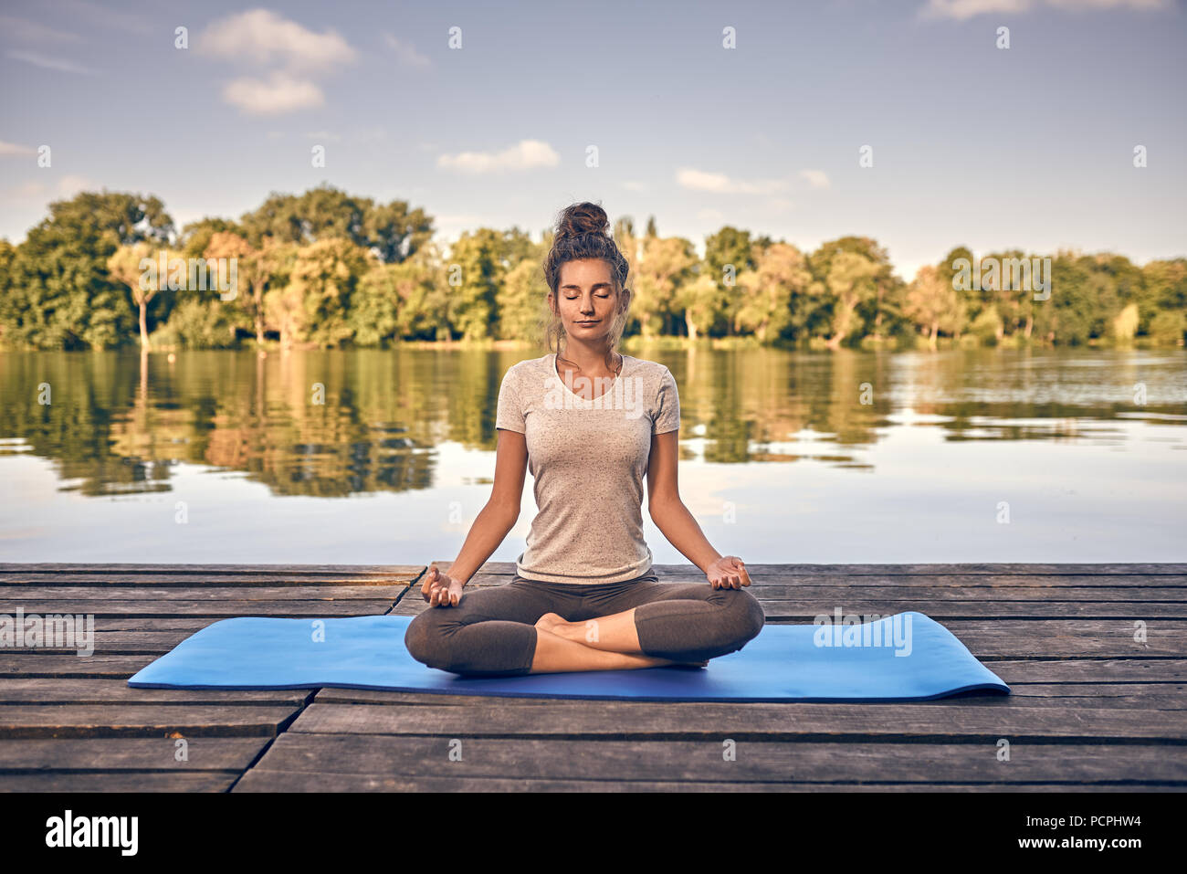 Smiling woman sitting meditating on a wooden deck Stock Photo