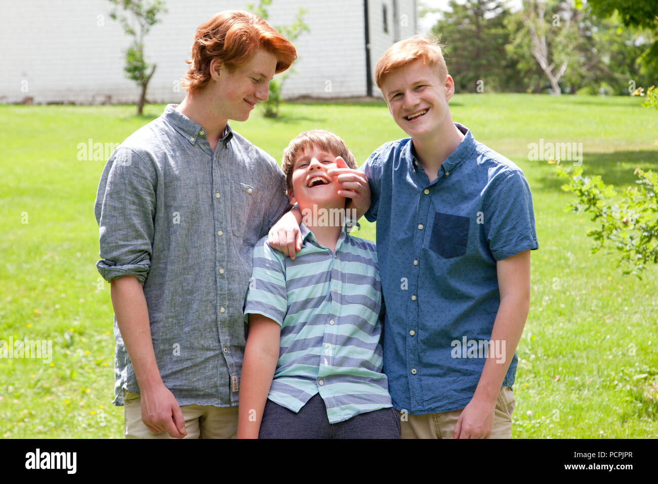 Three ginger siblings laugh and horse around outside, picking on the youngest Stock Photo