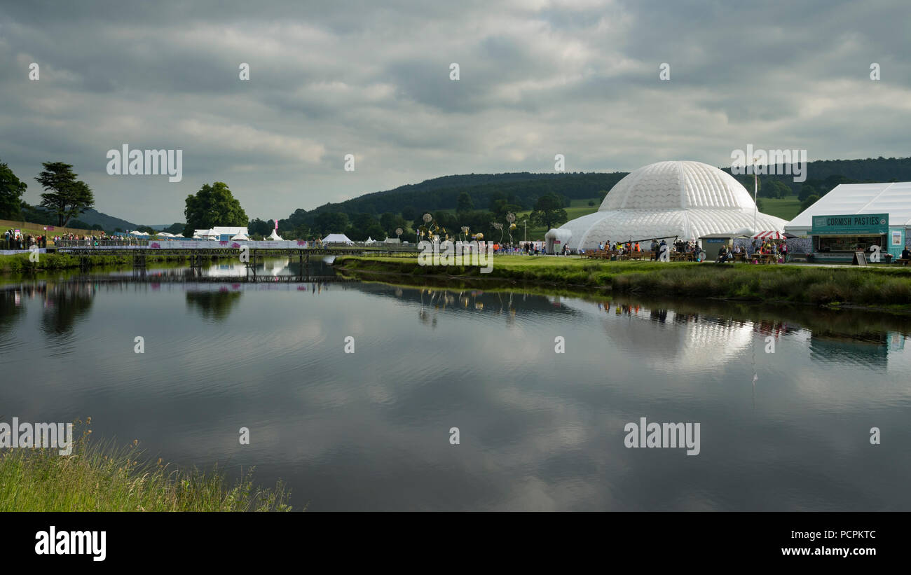RHS Chatsworth Flower Show showground (people visiting, marquee, tents, Great Conservatory dome & bridge reflected in river) Derbyshire, England, UK. Stock Photo