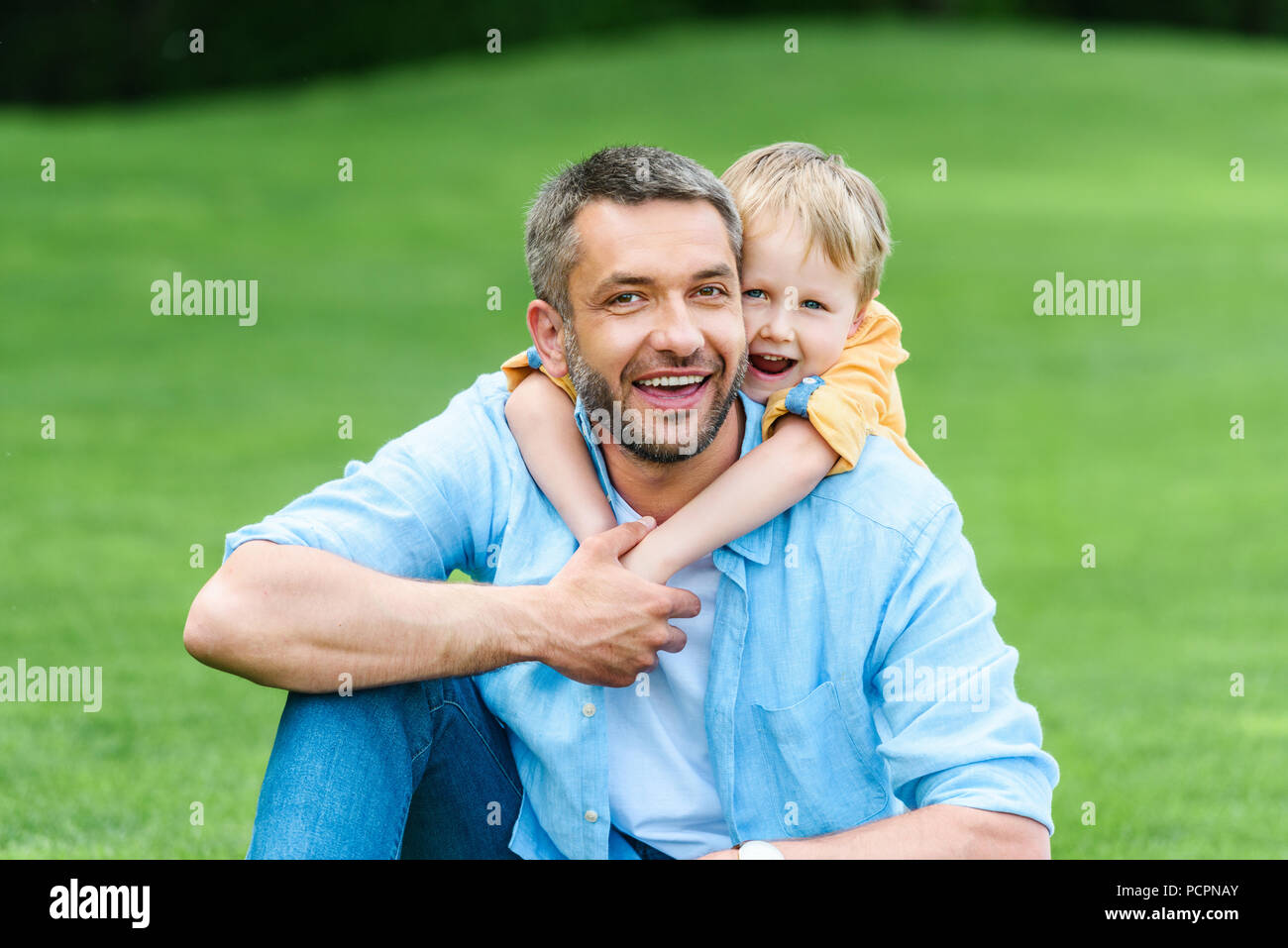 happy father and son hugging and smiling at camera in park Stock Photo ...
